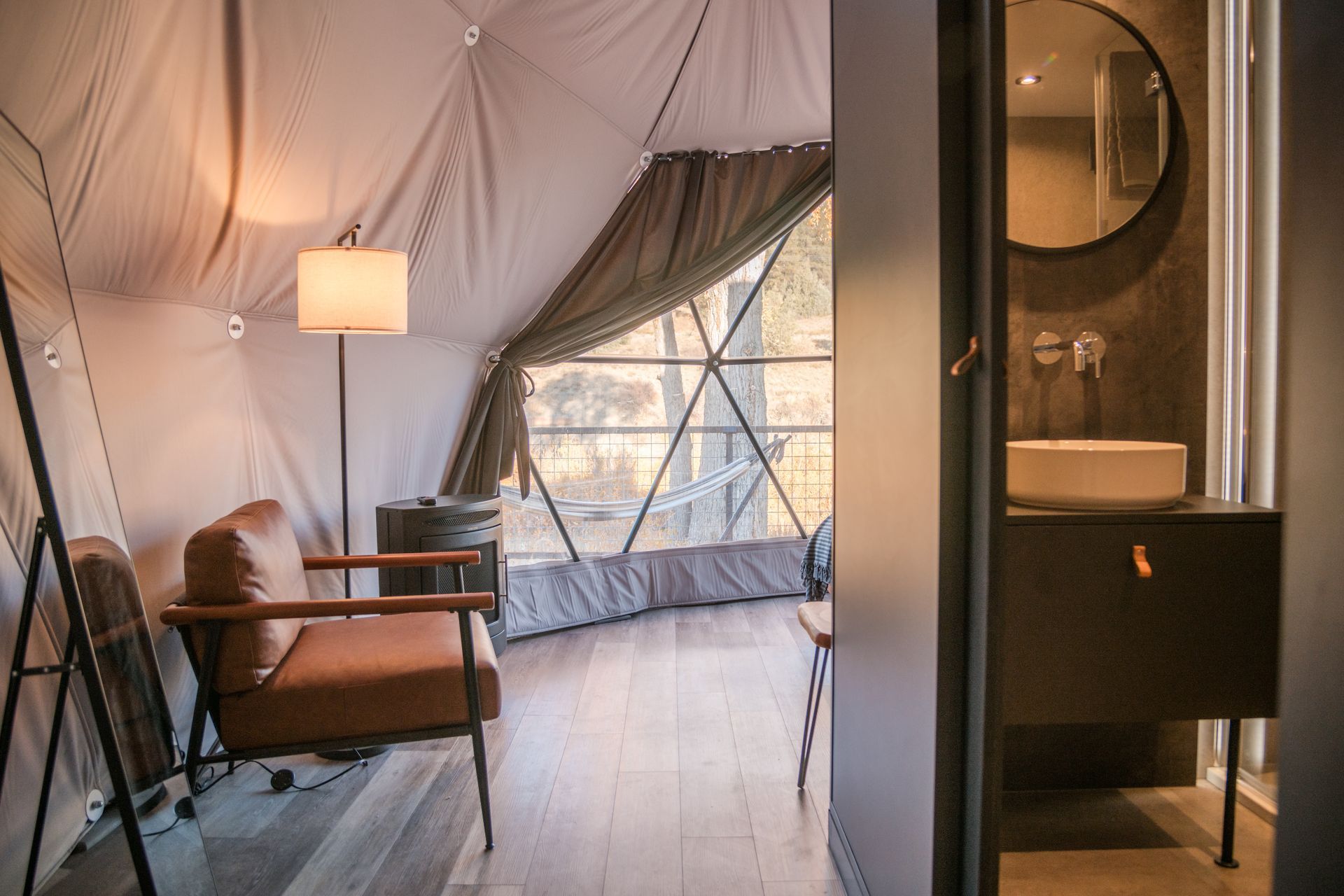 Interior of a glamping dome with seating area, window, and bathroom.