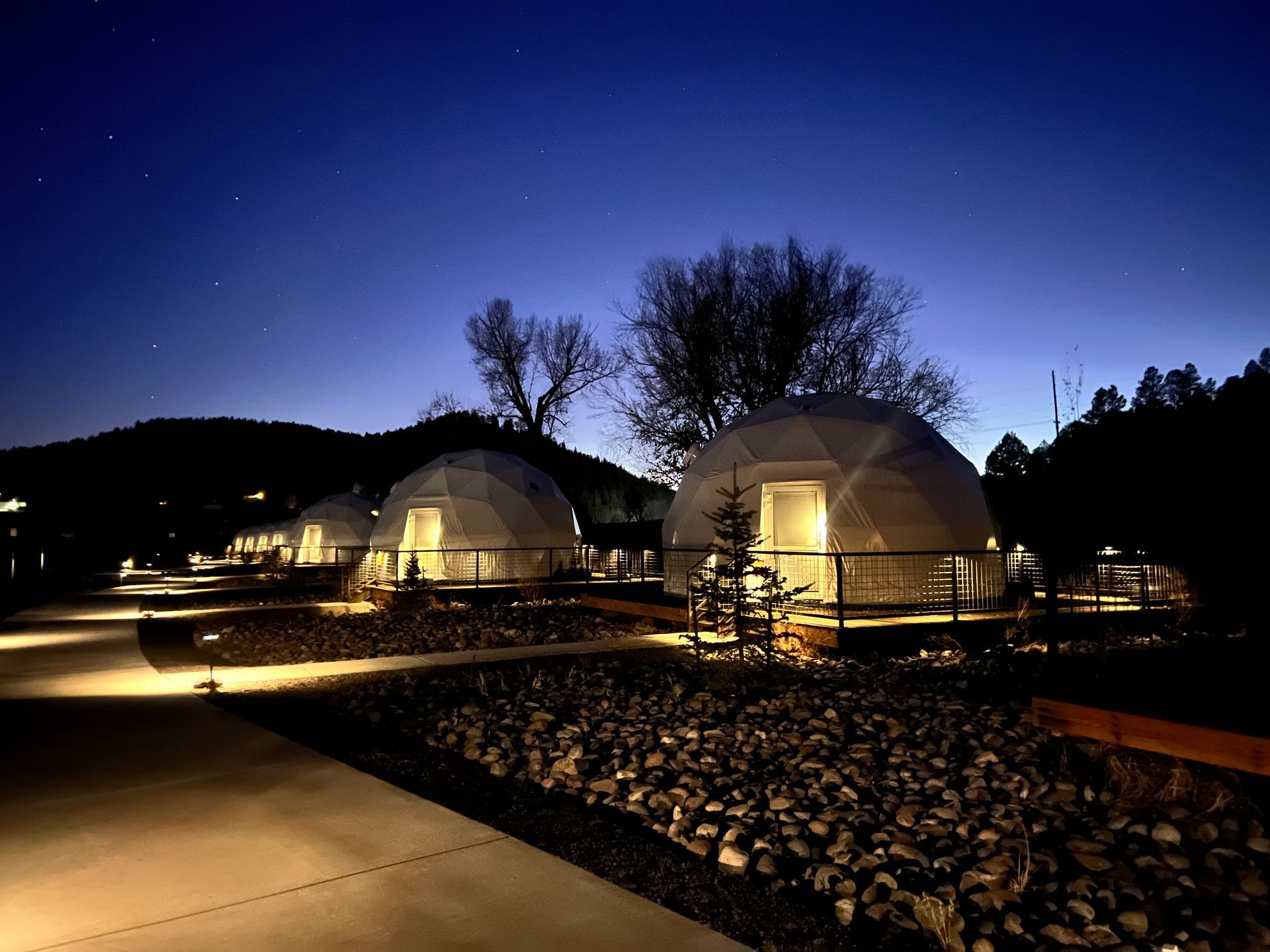 Night view of illuminated geodesic domes with a starry sky and a paved walkway.