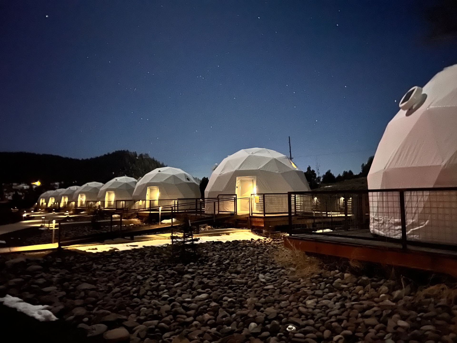 Geodesic domes, lit at night, line a rocky shore under a dark, starry sky.