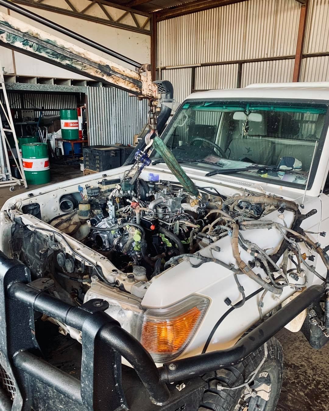 White car with the engine removed, inside a workshop. A crane lifts the engine — Traction Diesel Services in Clermont, QLD