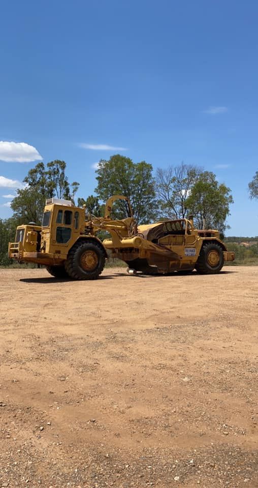 Yellow Earth Scraper Parked on Dirt Under a Blue Sky — Traction Diesel Services in Clermont, QLD