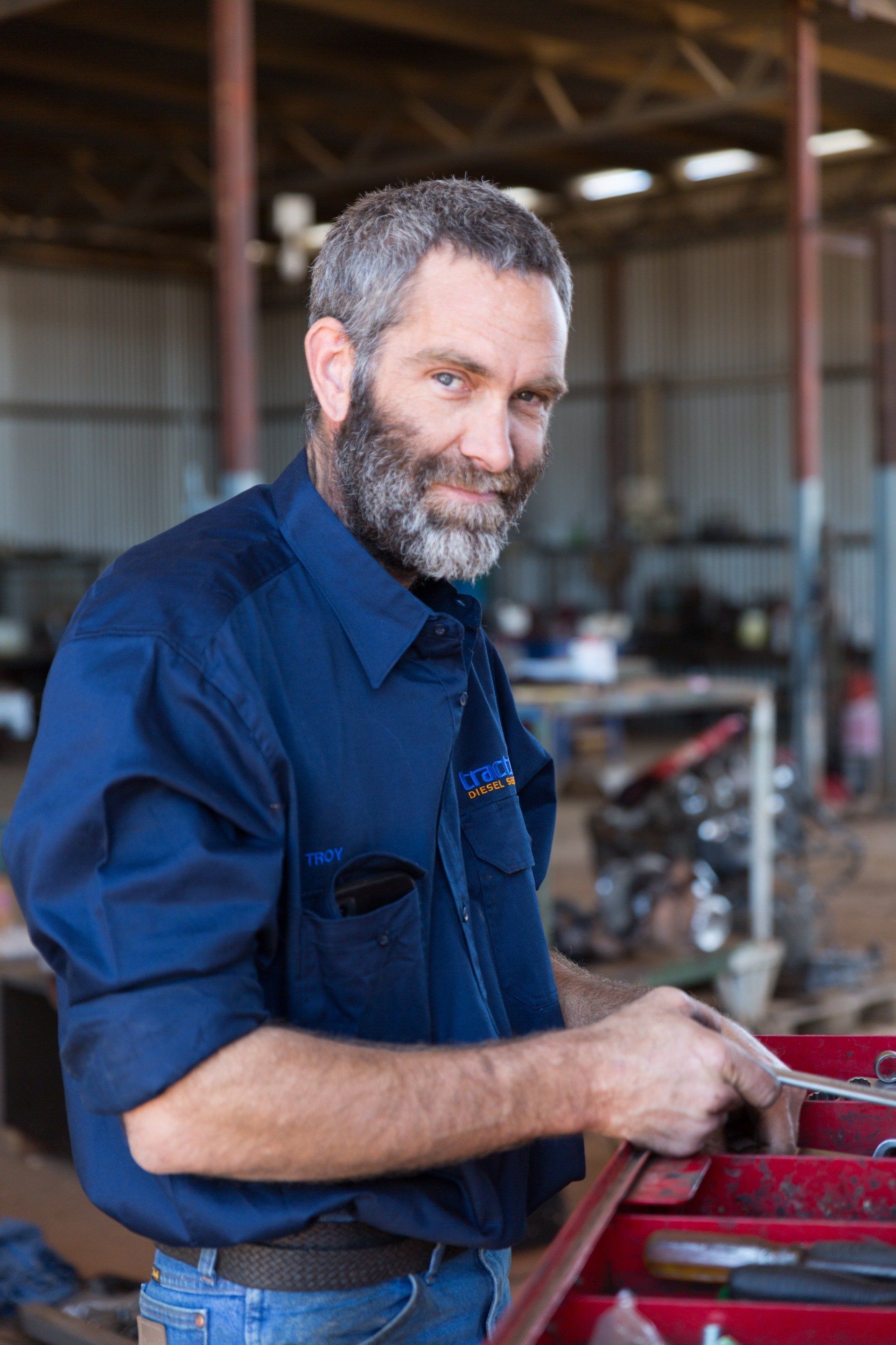 Mechanic in Blue Work Shirt Smiles, Leans on Toolbox in Garage — Traction Diesel Services in Clermont, QLD