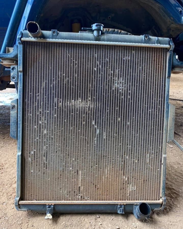 Dirty, Rectangular Car Radiator With Metal Fins; Upper and Lower Hoses Visible — Traction Diesel Services in Clermont, QLD