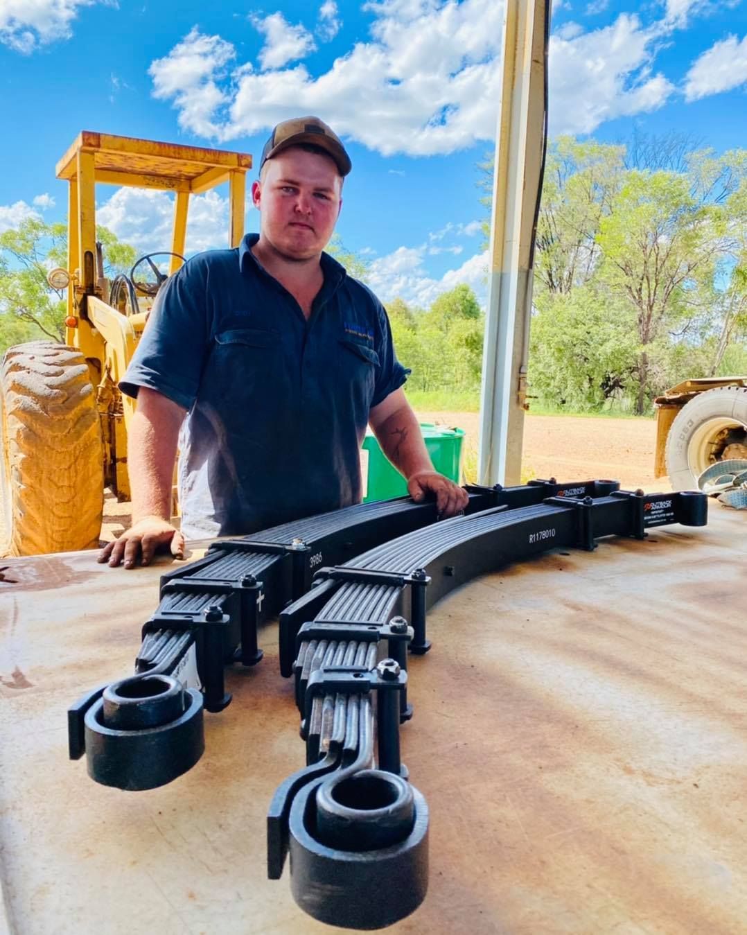 Man Holding Two Large Black Leaf Springs Outside — Traction Diesel Services in Clermont, QLD