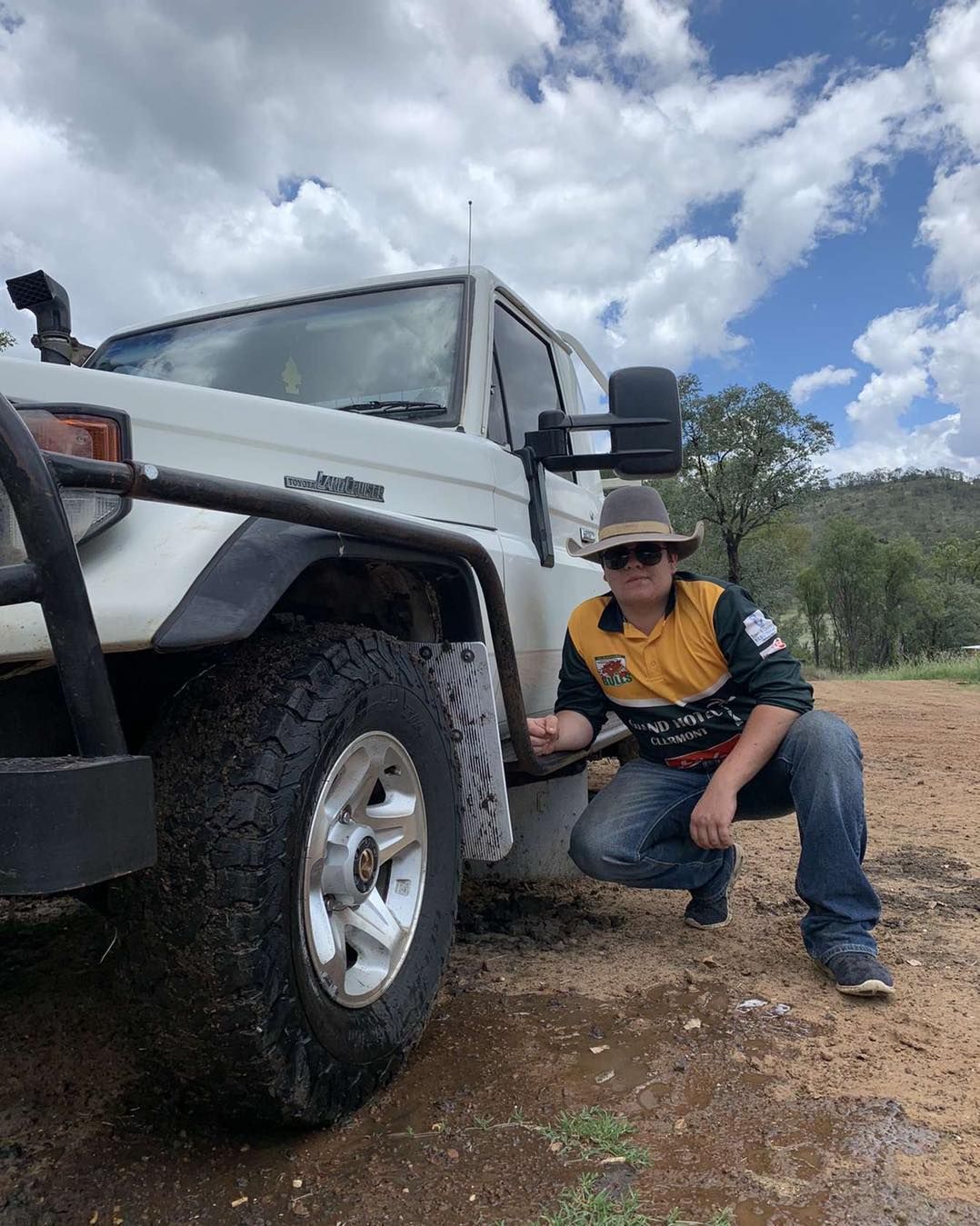Man Crouches Beside a White Off-road Vehicle in a Natural Setting — Traction Diesel Services in Clermont, QLD