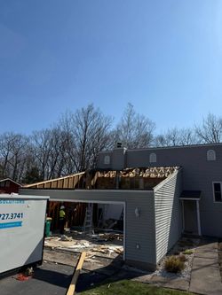 Damaged garage under repair with exposed wooden roof framing and debris in front