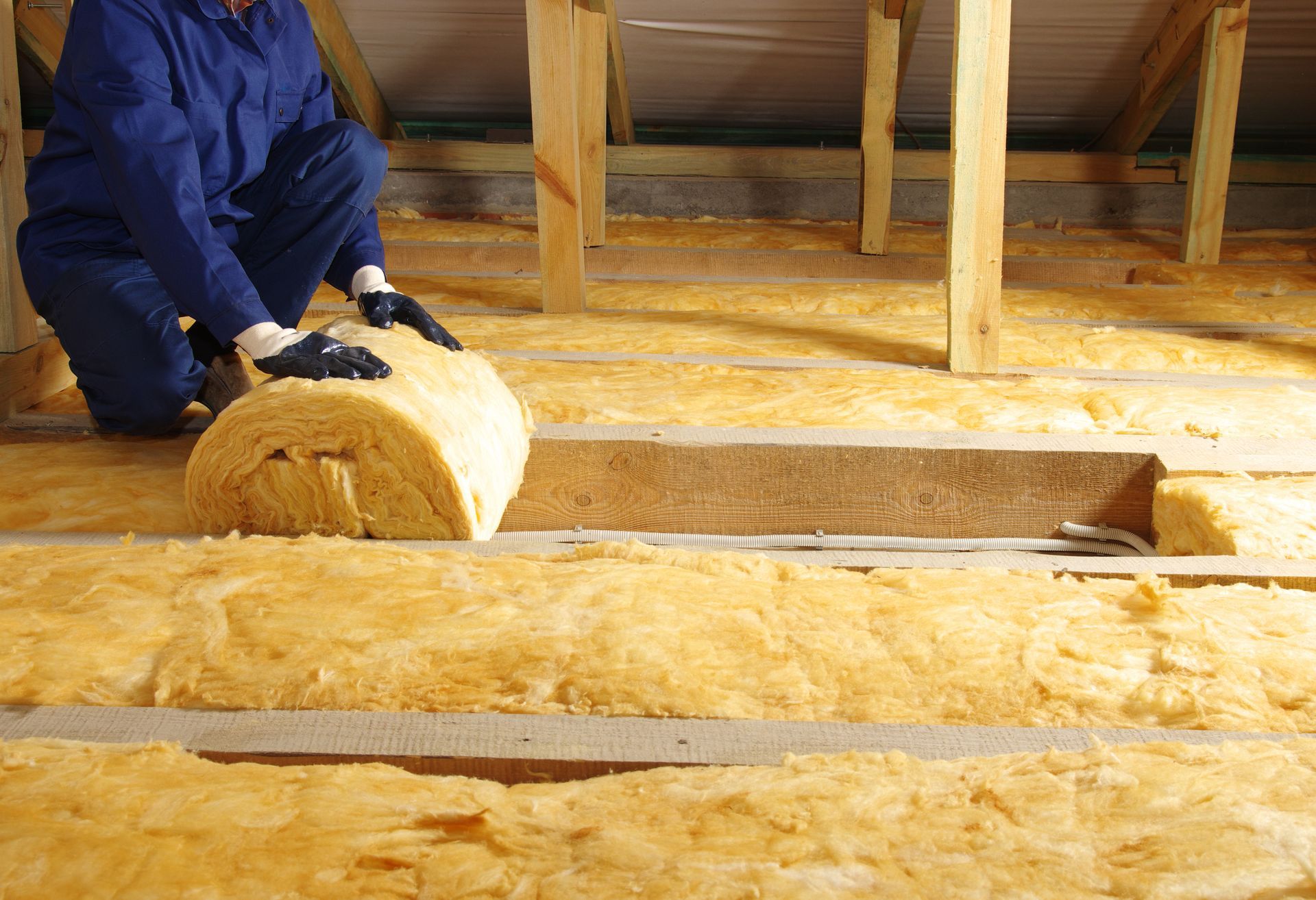 Worker rolling yellow insulation batts in an attic under construction