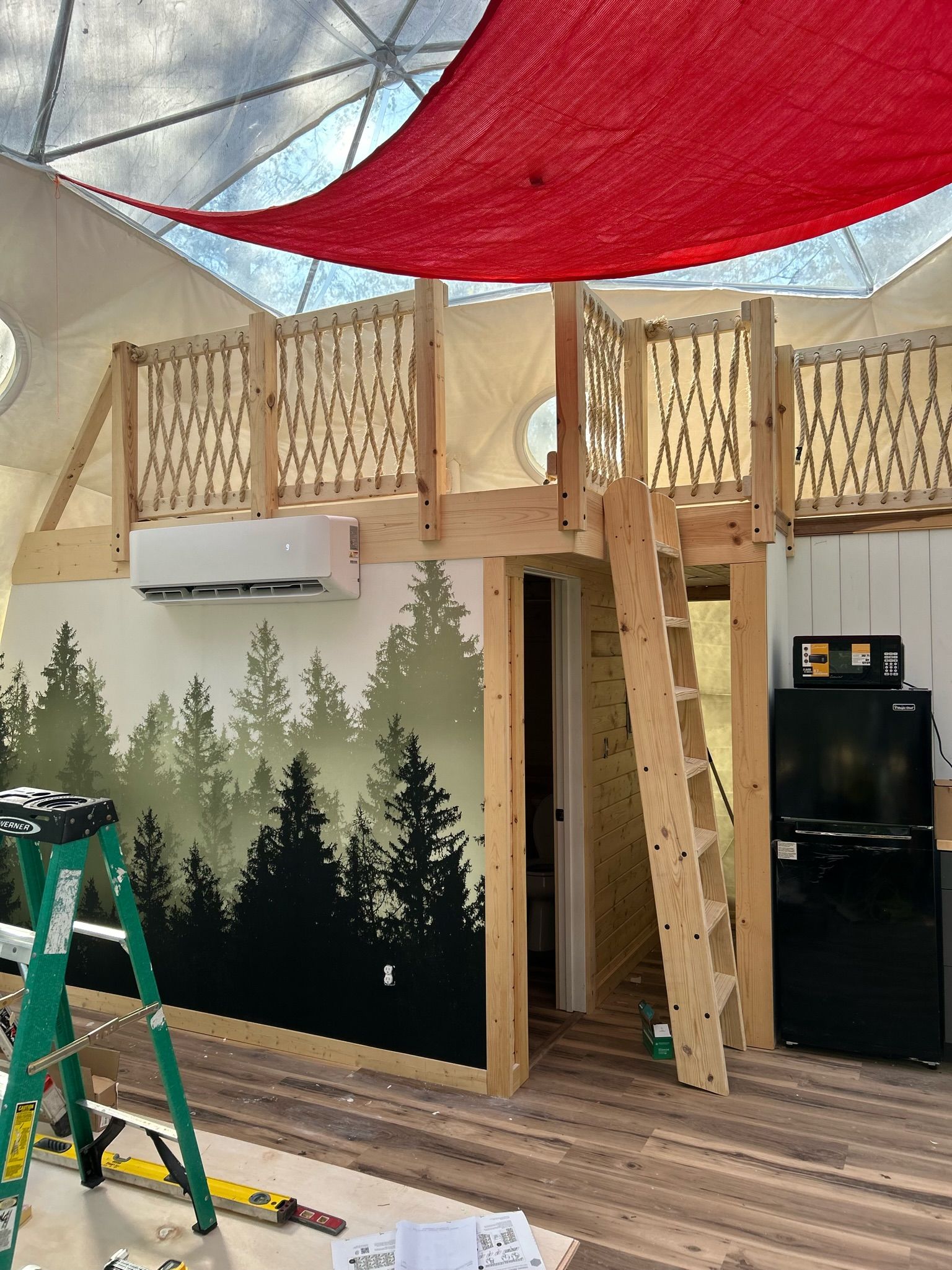 A room with a ladder and a painting of trees on the wall