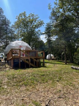A dome tent with a deck in the middle of a field surrounded by trees.