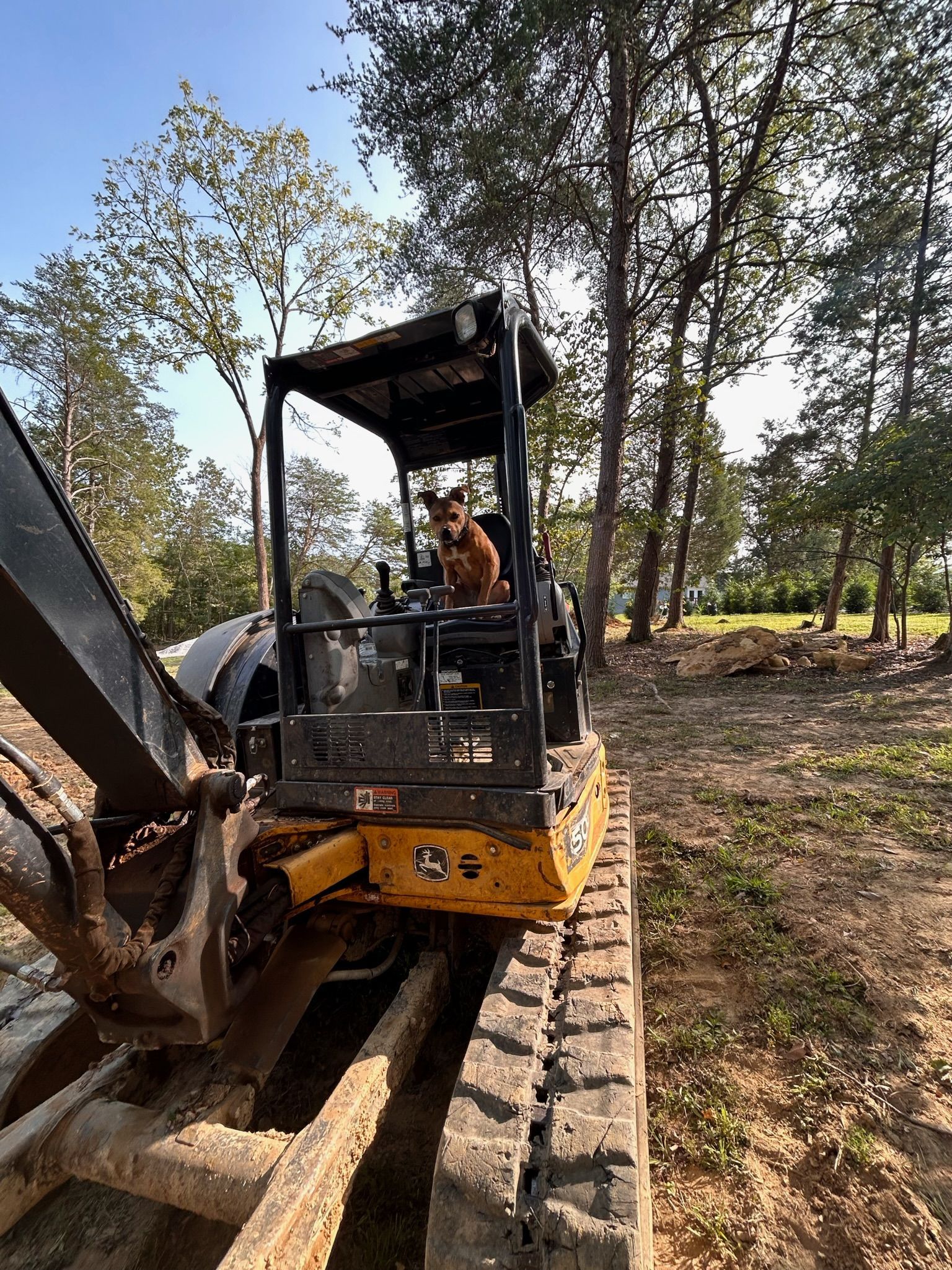 A man is driving a bulldozer in a field with trees in the background.