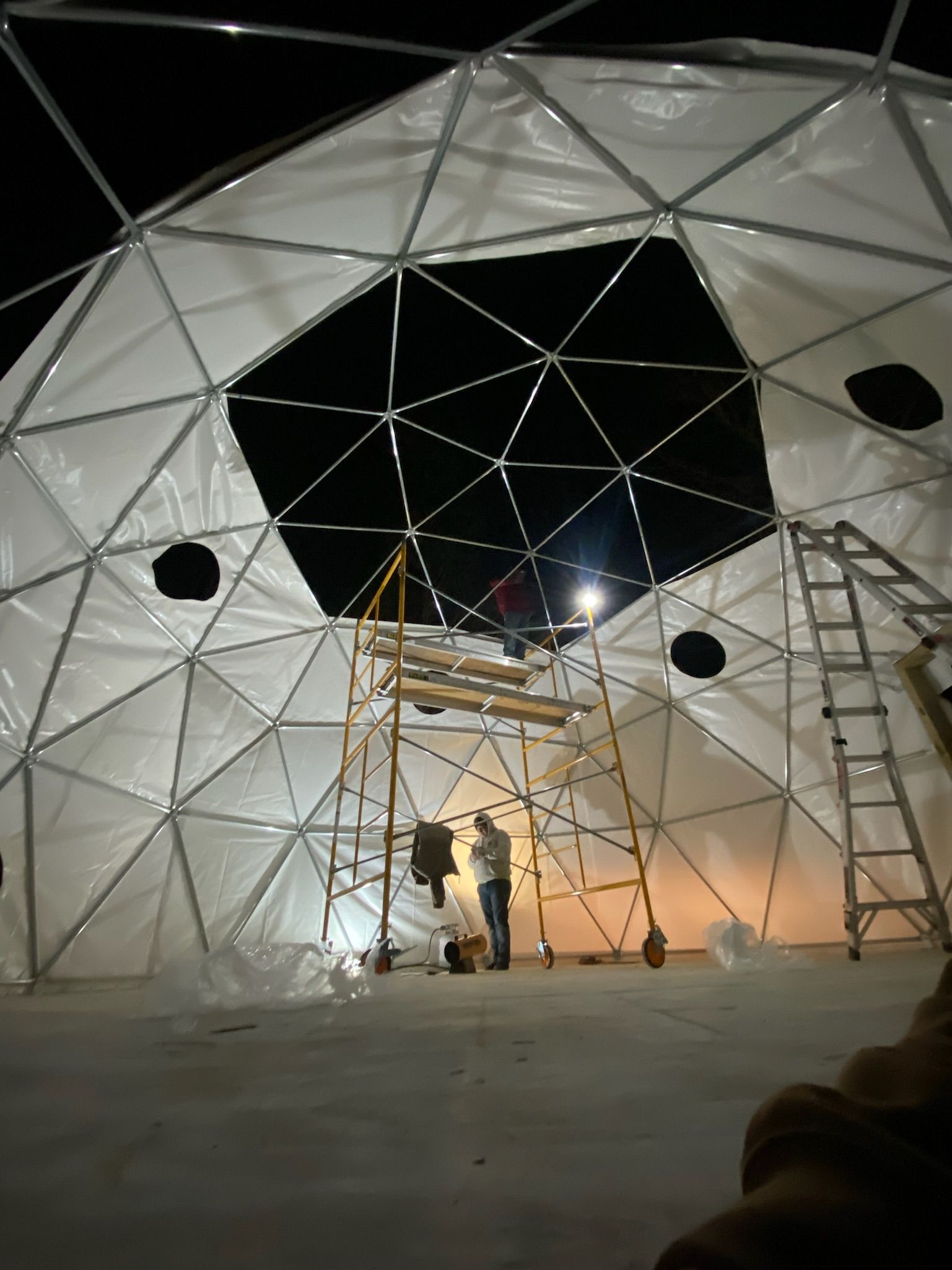 A man is standing on a ladder inside of a dome at night.
