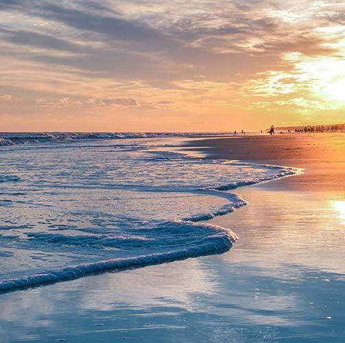 Sunset over the ocean. Waves roll onto the beach, reflecting the orange sky.