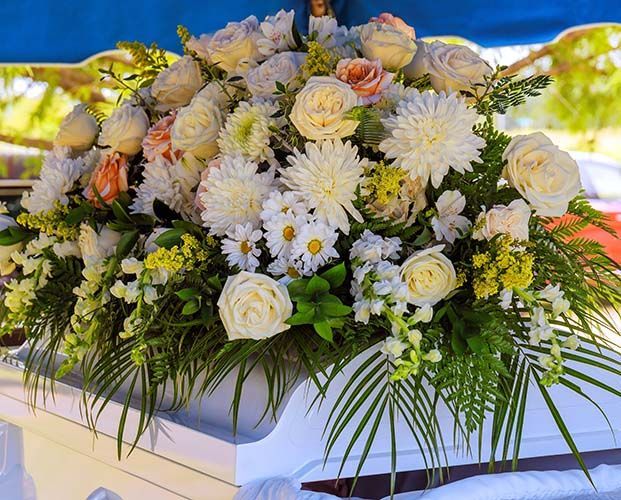 Floral arrangement on a white surface, featuring white roses, daisies, and green foliage.