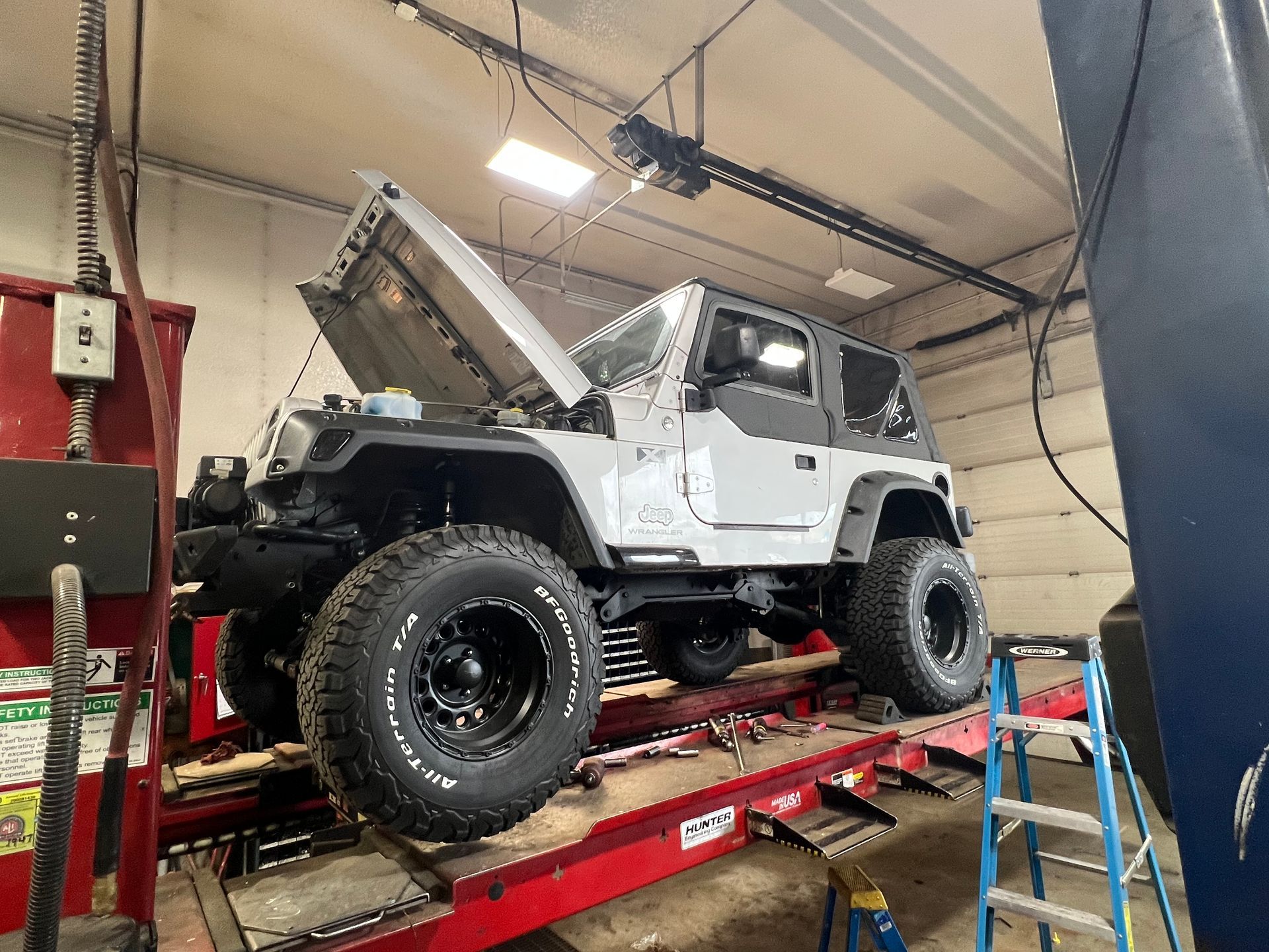 A jeep is sitting on a lift in a garage with its hood up.