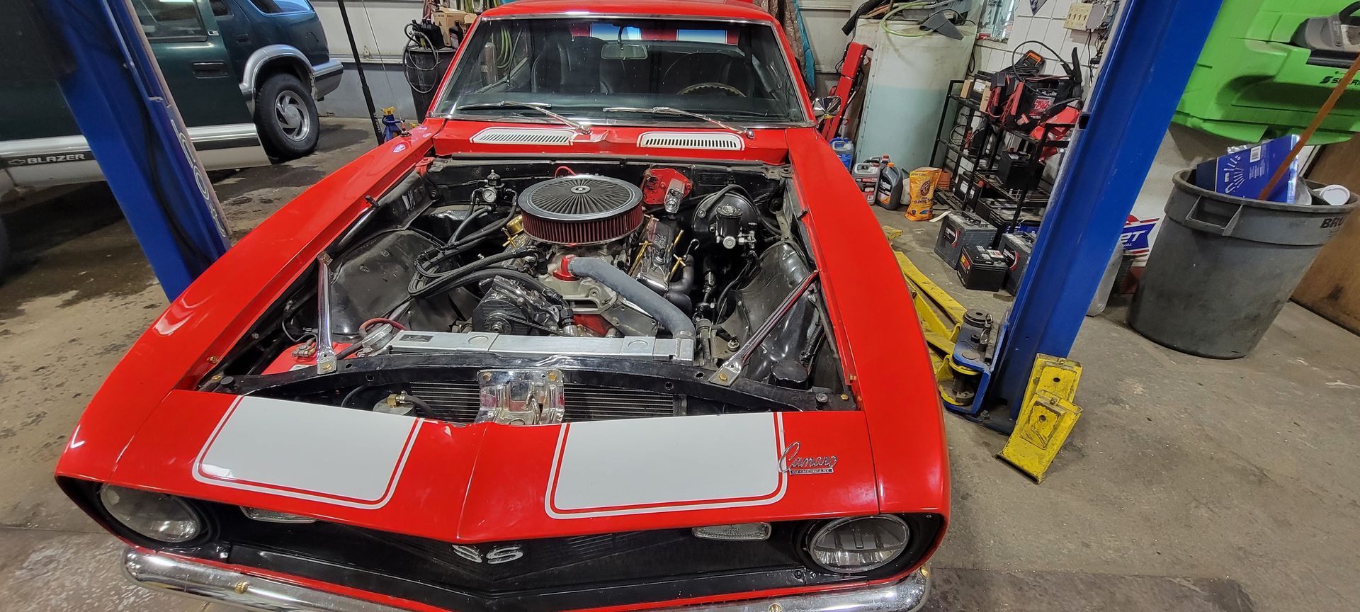 A red car with the hood open is on a lift in a garage.