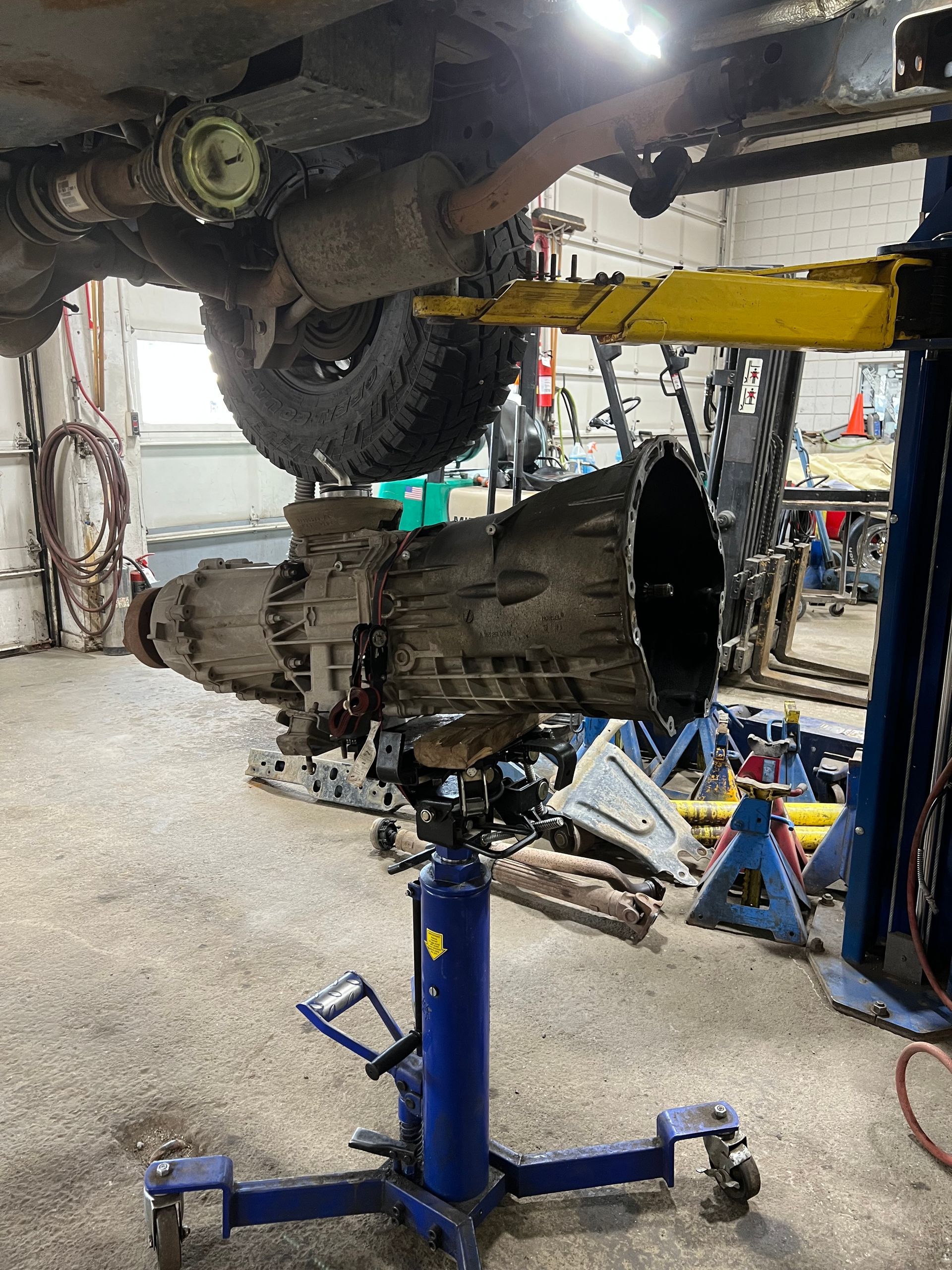 A car is being worked on in a garage with the transmission removed