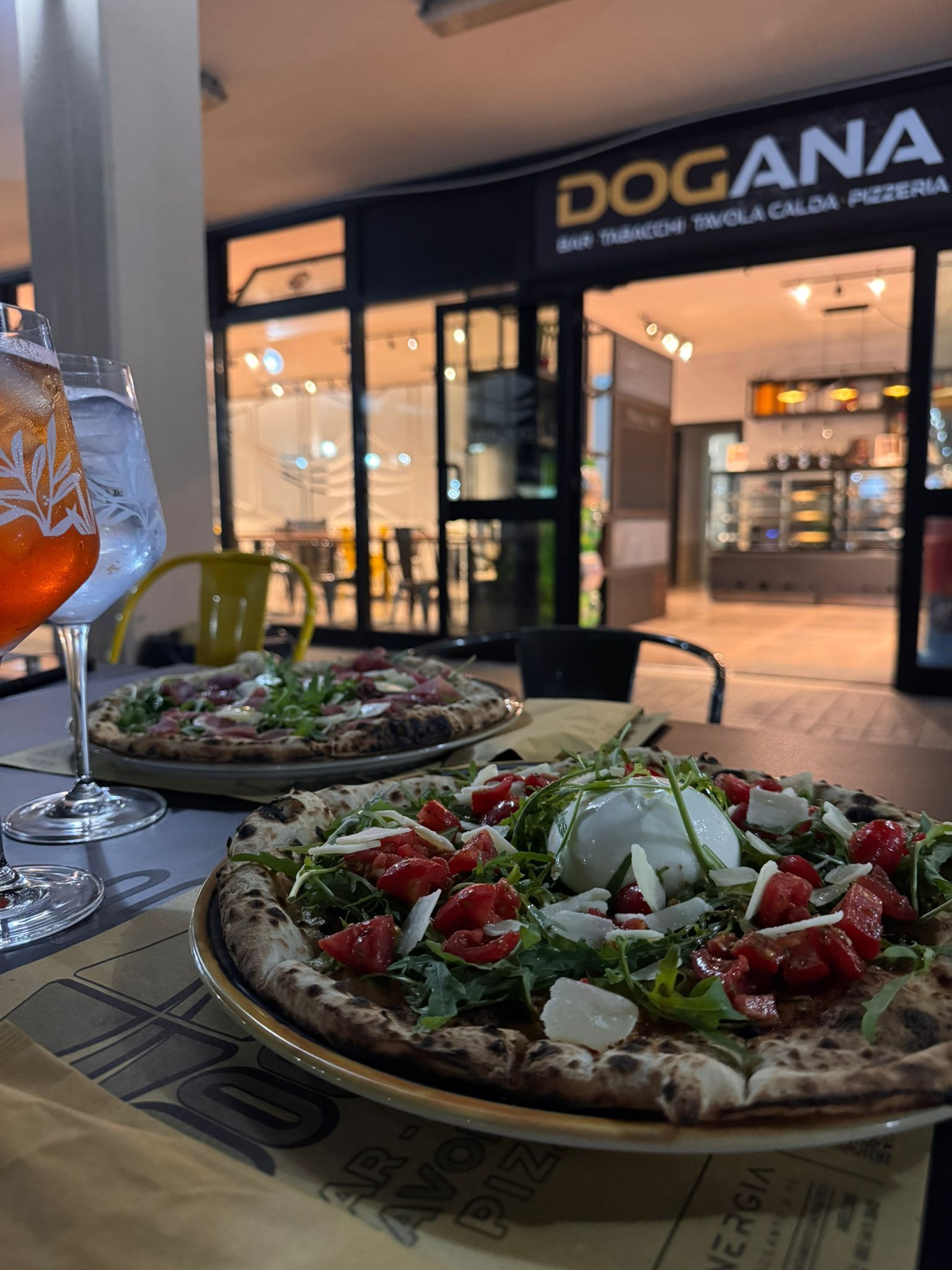 Due pizze sono appoggiate su un tavolo davanti a un negozio chiamato dogana