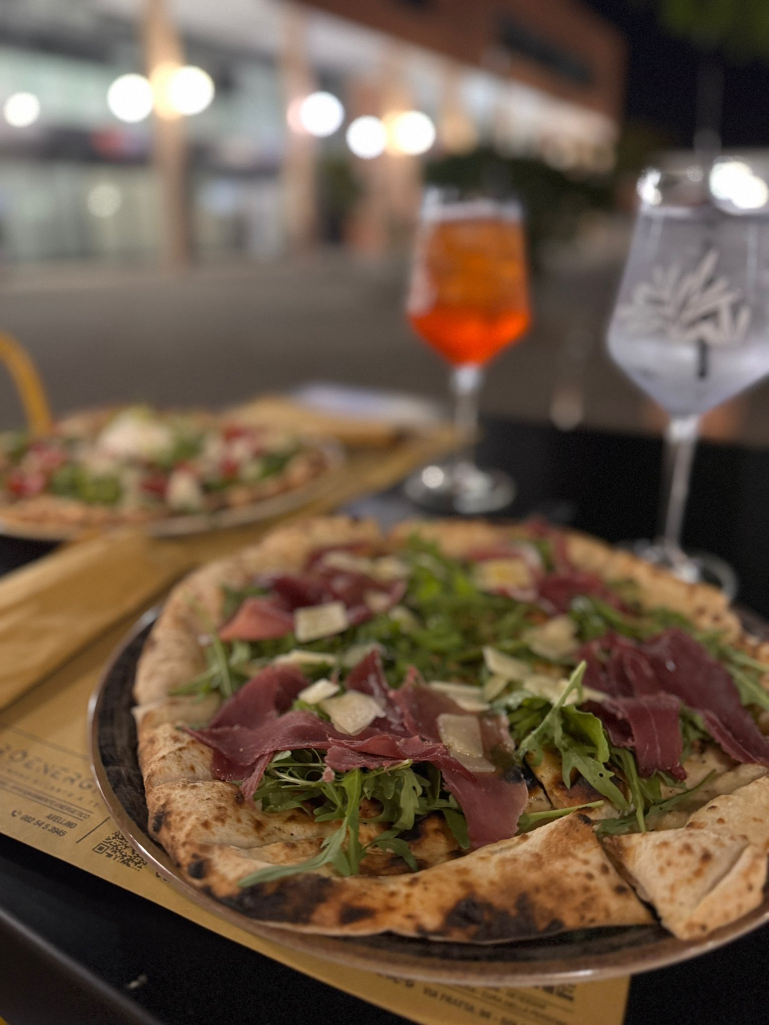 Una pizza è appoggiata su un vassoio accanto a un bicchiere di vino.