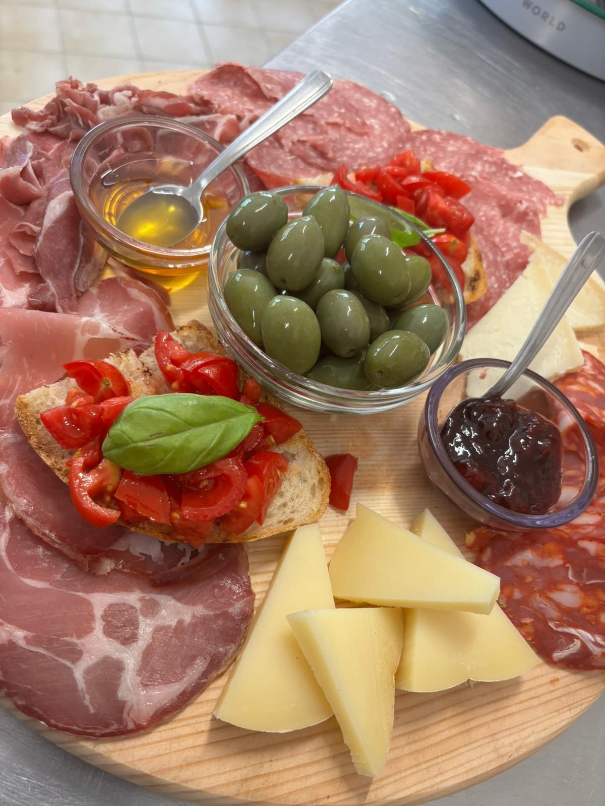 Un tagliere di legno con sopra carne, formaggio, olive, pomodori e marmellata.