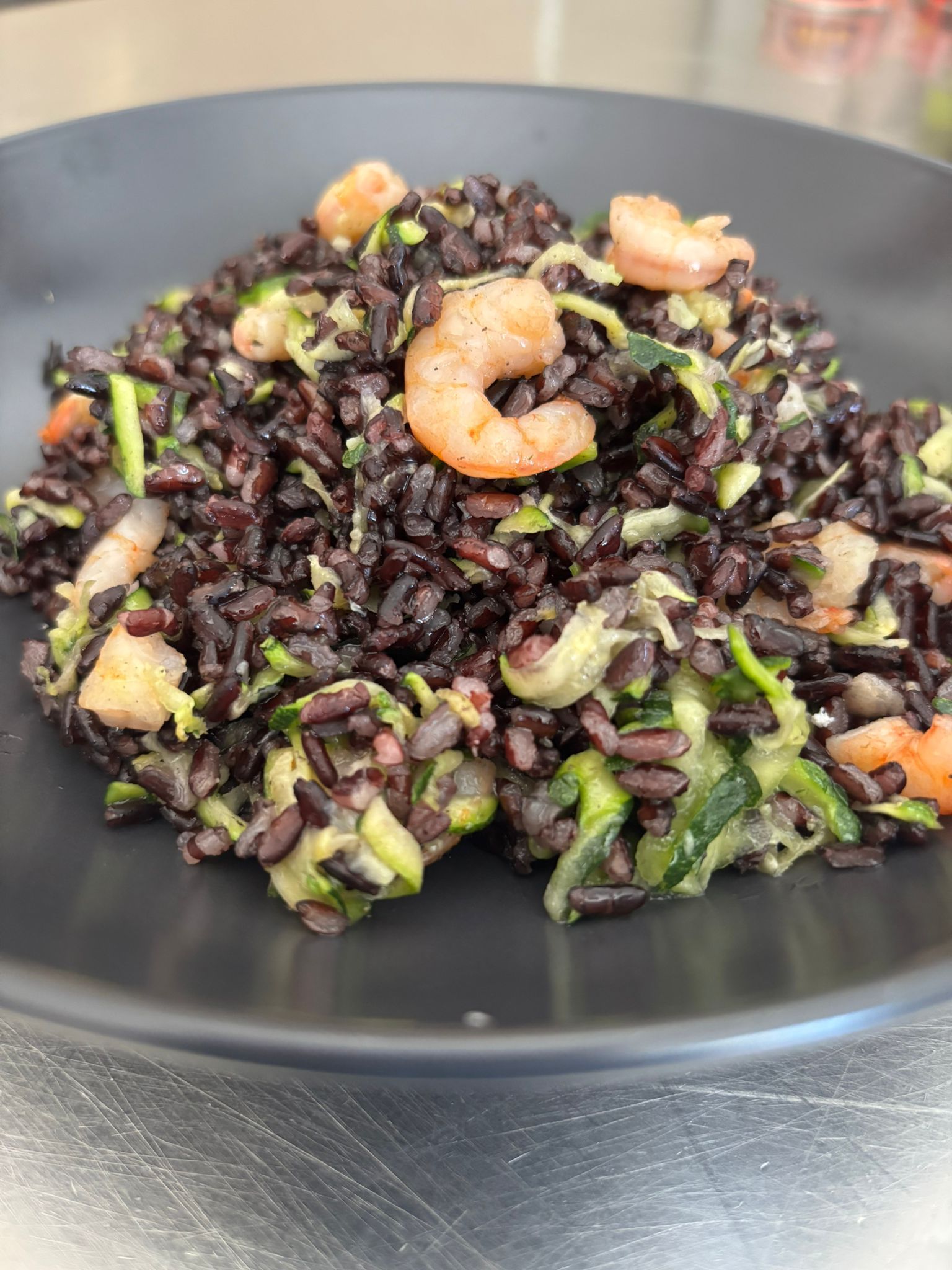 Un piatto nero con riso e gamberi su un tavolo.