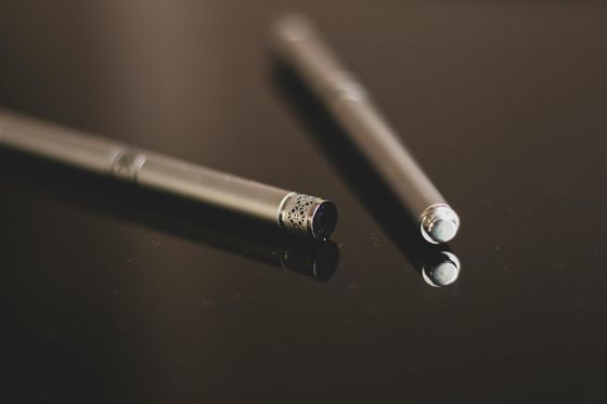 Two electronic cigarettes are sitting on a black surface.