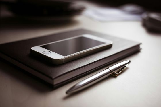 A cell phone sitting on top of a notebook next to a pen