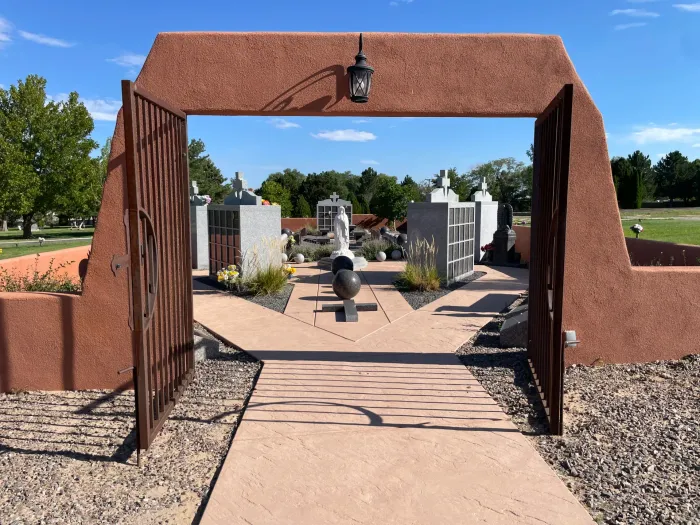 Rendering of a memorial with a central cross and surrounding structures, trees, and sky.