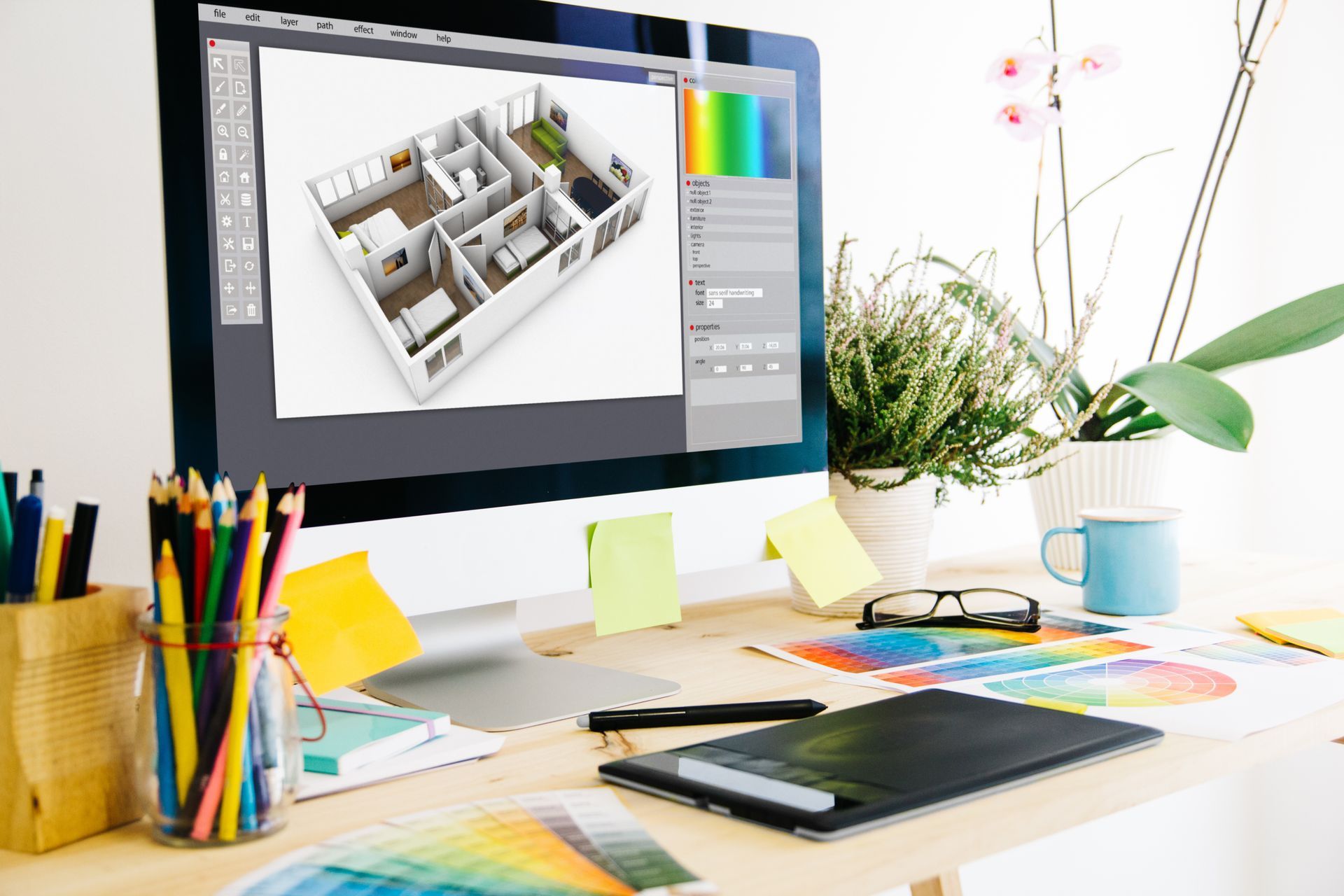 Computer screen displaying 3D interior design, with color swatches and art supplies on the desk.
