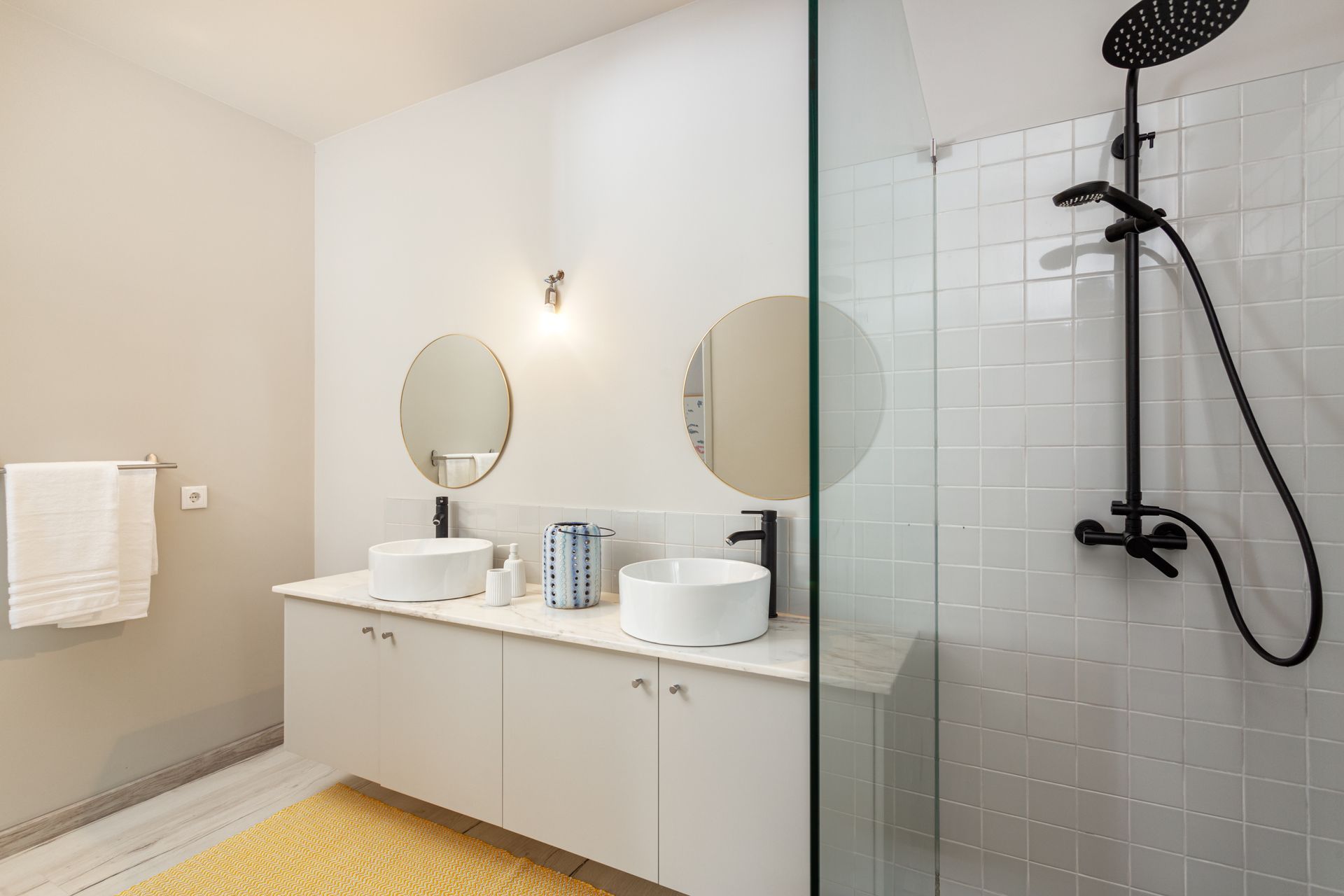 Modern bathroom with white cabinets, two round mirrors, black fixtures, and a glass shower.