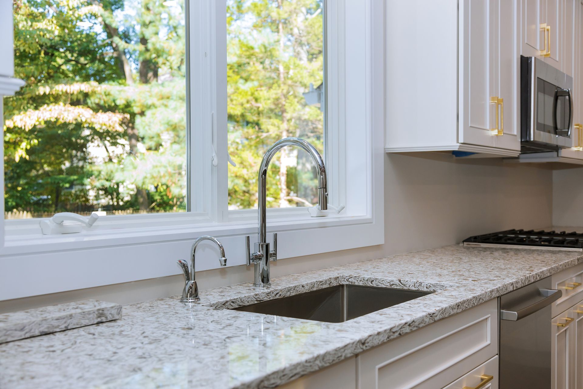 Kitchen with white cabinets, granite countertop, stainless steel sink and faucet, window with a view of trees.
