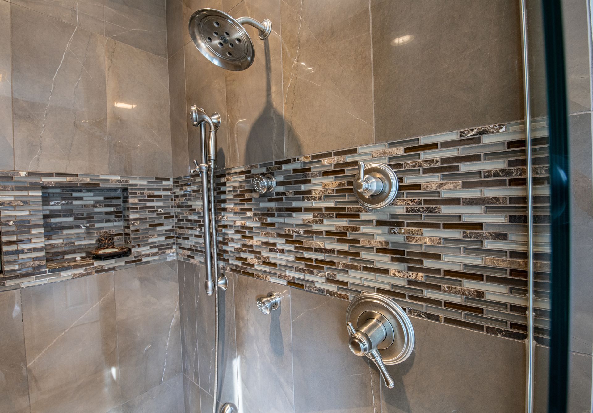 Modern shower with glass door, tiled walls, and multiple chrome showerheads.