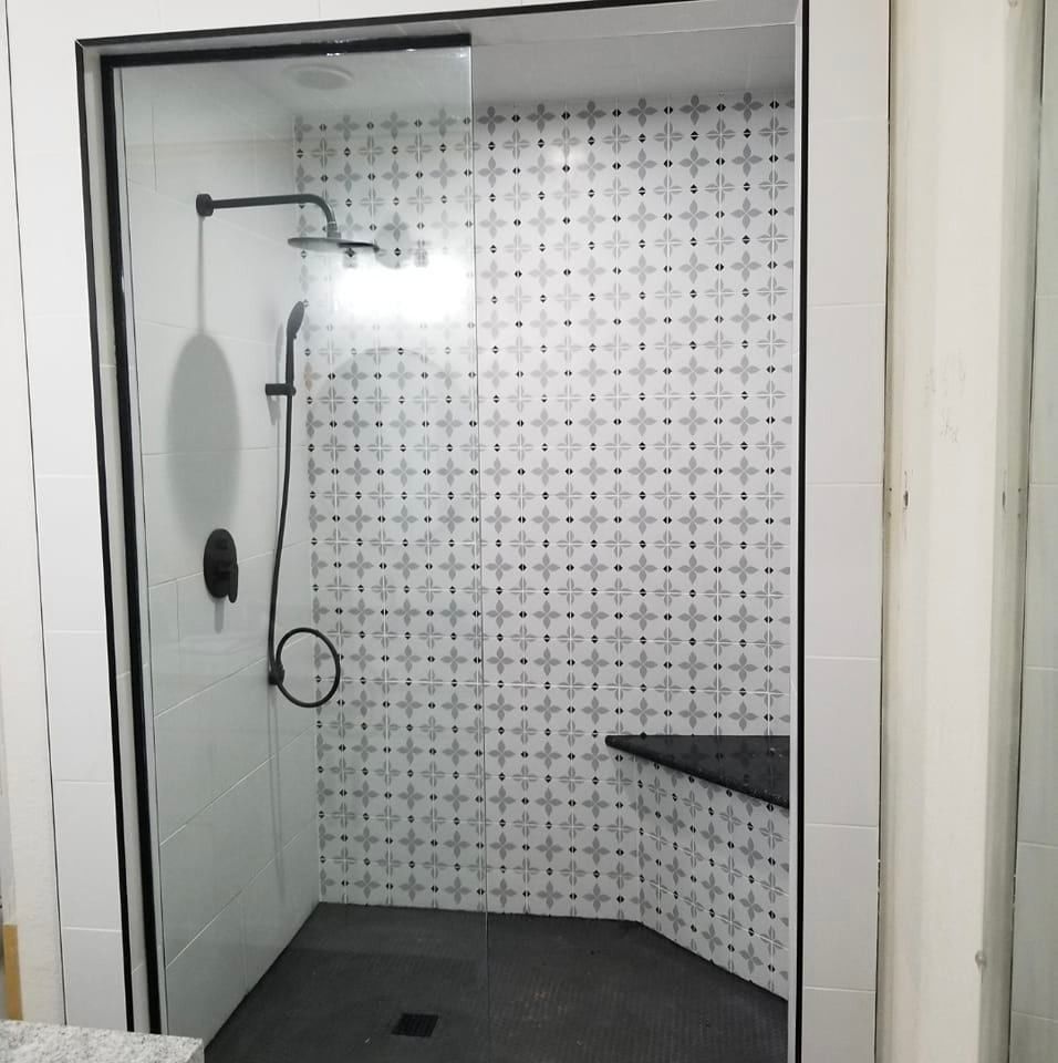 Modern shower with patterned tile, black fixtures, and glass door.