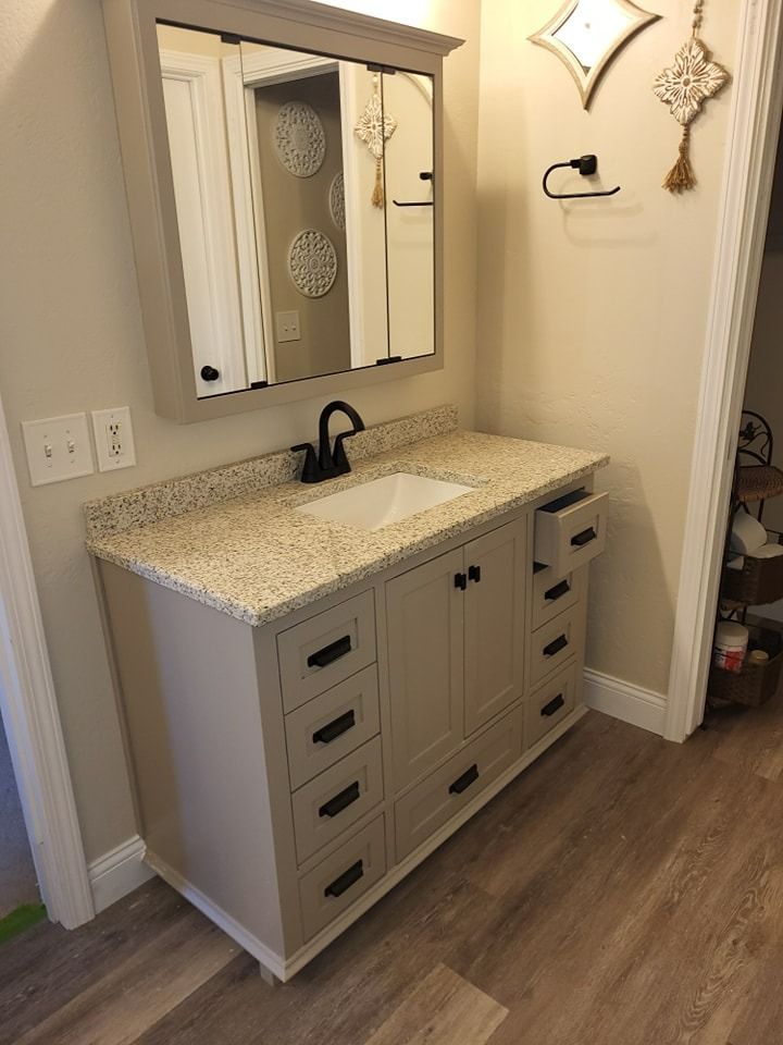 A bathroom vanity with beige granite countertop, black fixtures, and a mirrored cabinet.