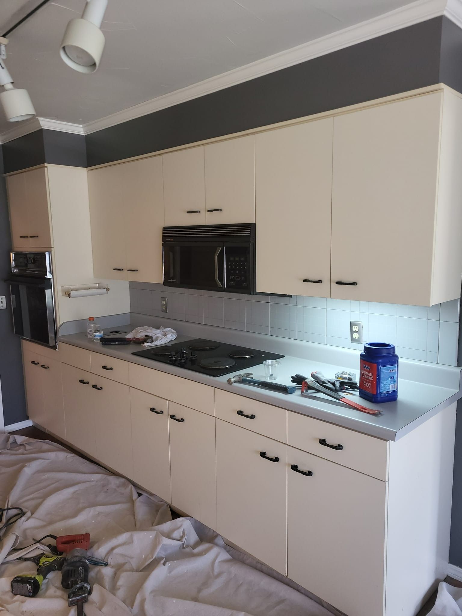 Cream kitchen cabinets with black hardware and a stainless steel oven and cooktop under a gray accent stripe.