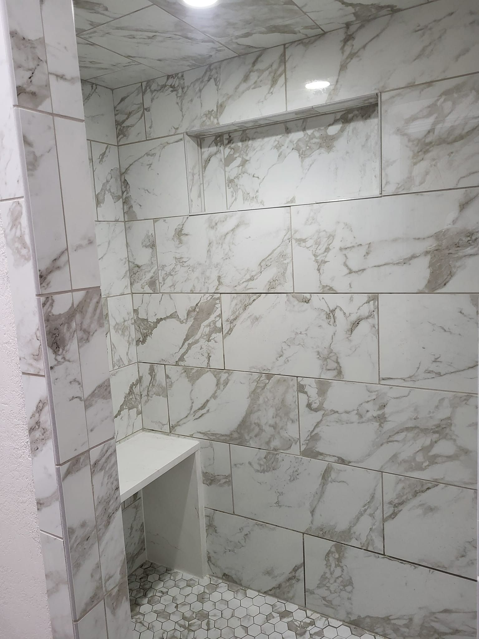 Marble-tiled shower with a built-in bench and shelf. White and gray veining throughout.