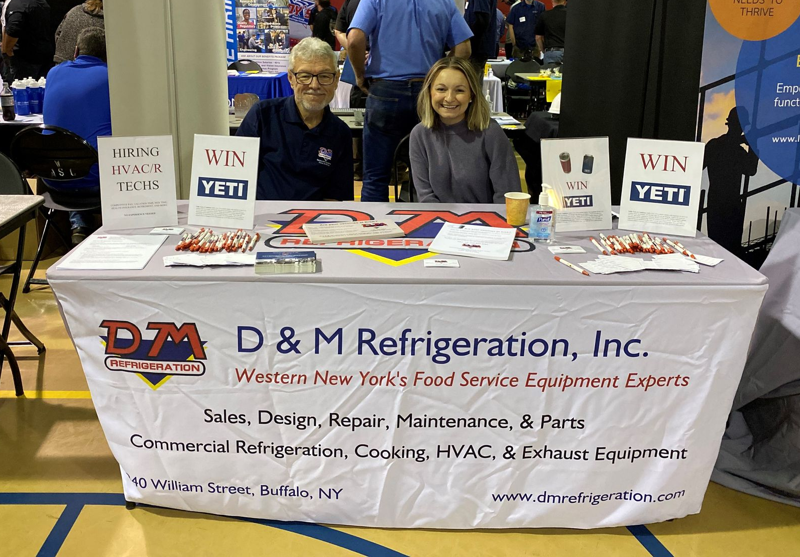 two men wearing masks stand in front of a sign for D&M Refrigeration