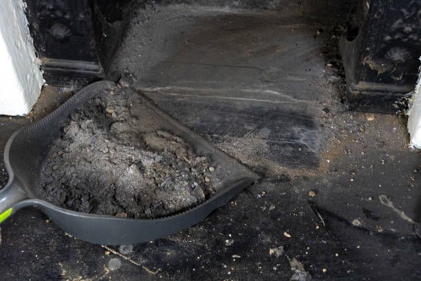 A shovel filled with dirt is sitting on the floor next to a fireplace.