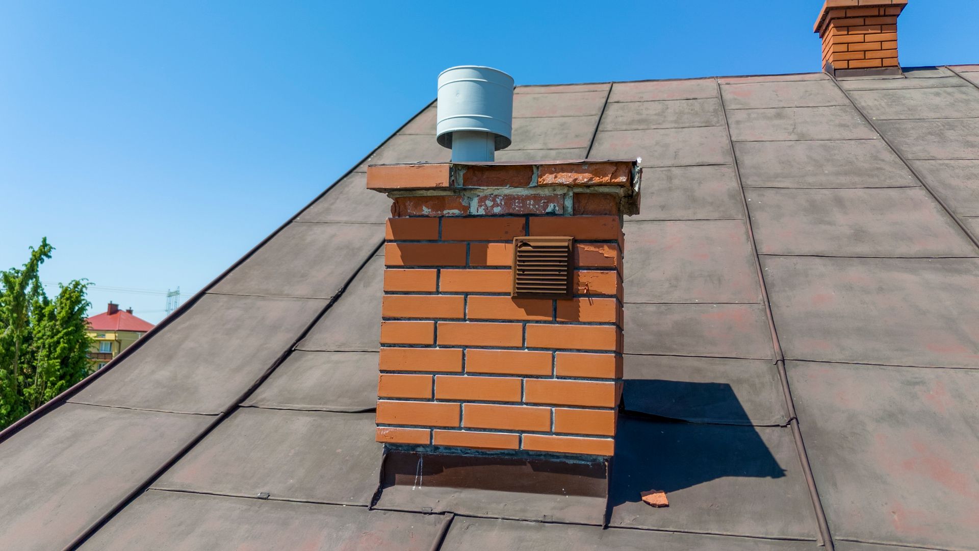 Brick chimney with metal cap on sloped roof under clear sky.