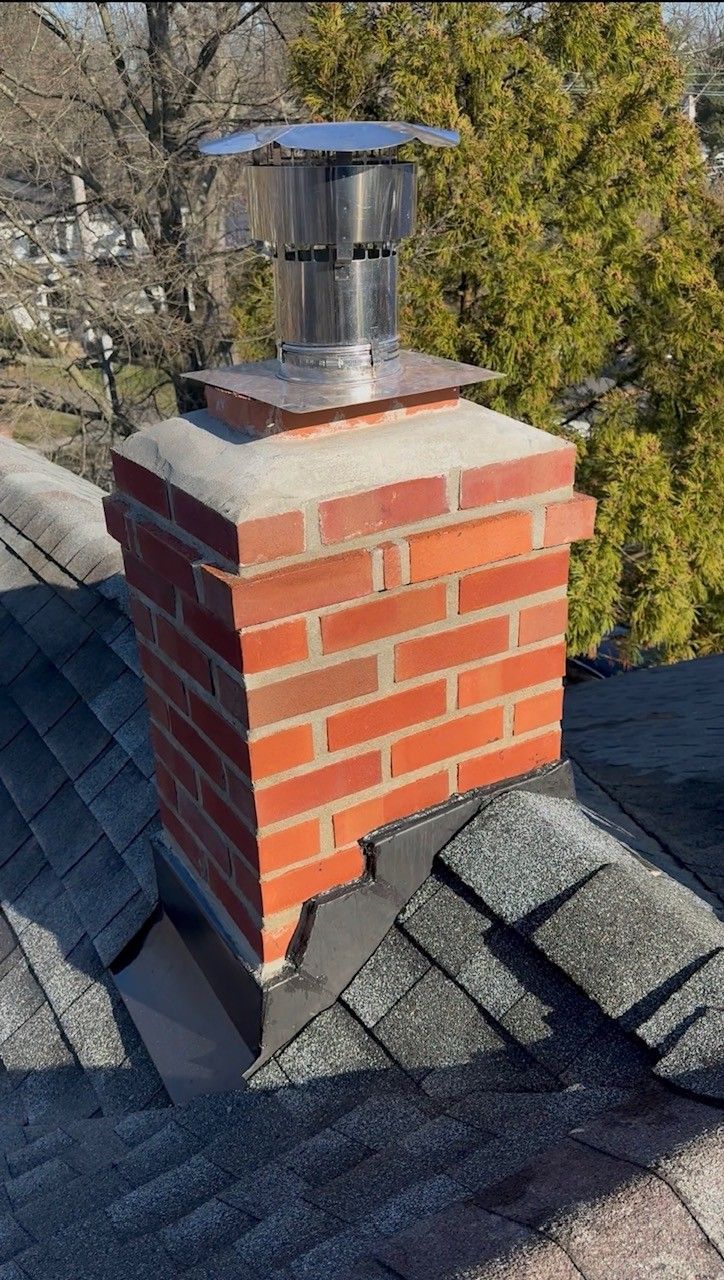 Two men are working on a chimney on a roof.