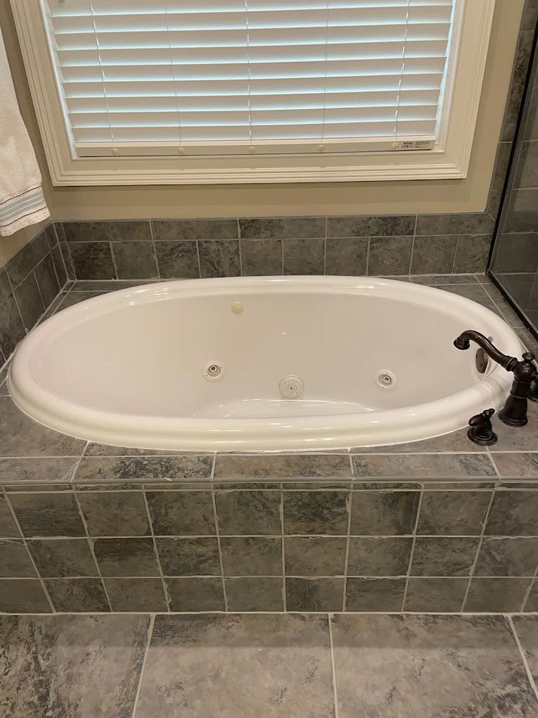 Oval bathtub with dark tile surround and window.