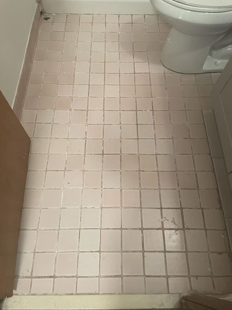 Pink tile bathroom floor with a toilet and cabinet in view.