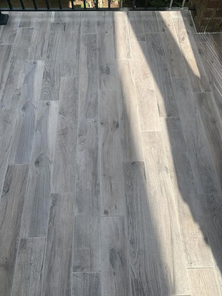 Light gray, wood-look tiled patio with a shadow cast across it.