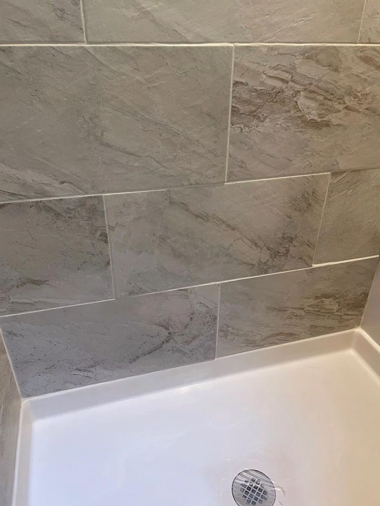 Gray tiled shower walls above a white shower base with a drain.
