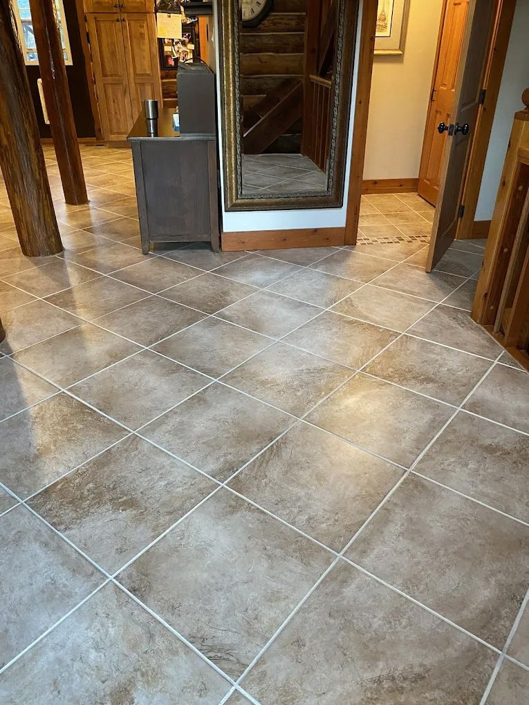 Brown tile floor with white grout in a home's entrance, leading to wooden stairs and a door.