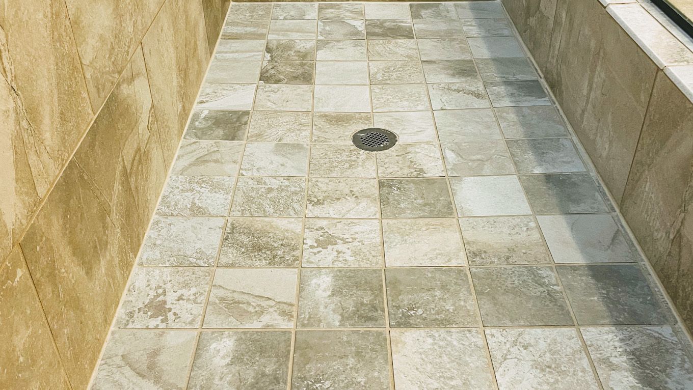 Shower floor tiled with gray and beige stone. Drain visible.