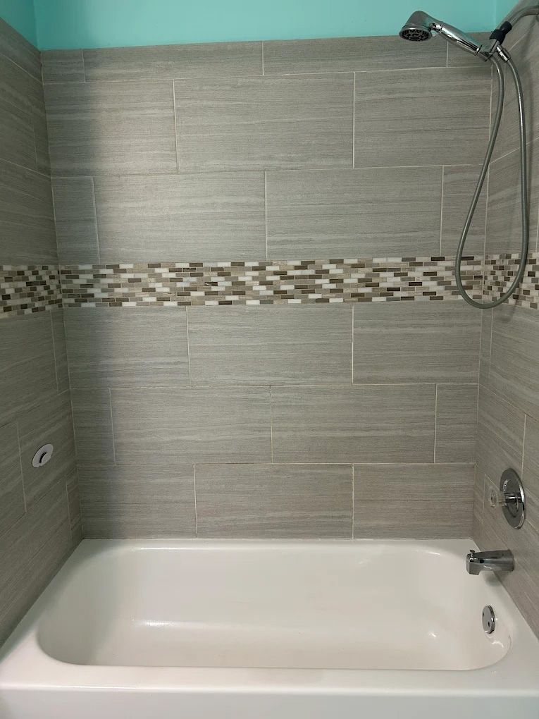 Gray tiled shower with a decorative mosaic band, white tub, and chrome fixtures.