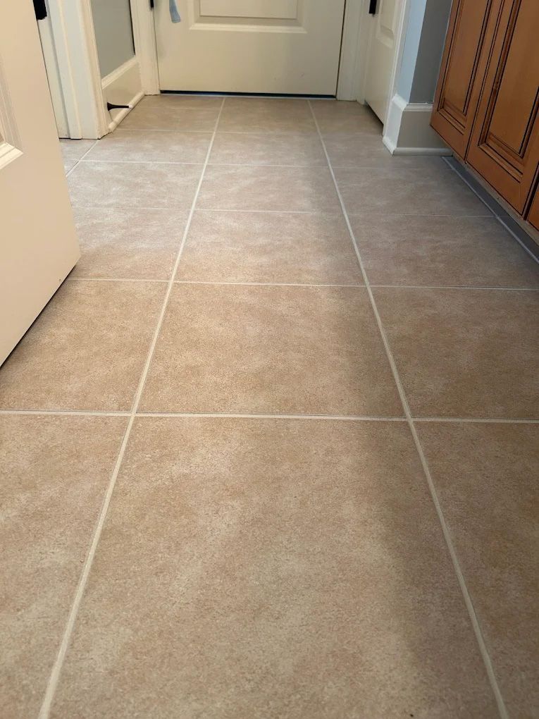 Beige tile floor in a hallway, leading to a white door. Cabinets on the right side.