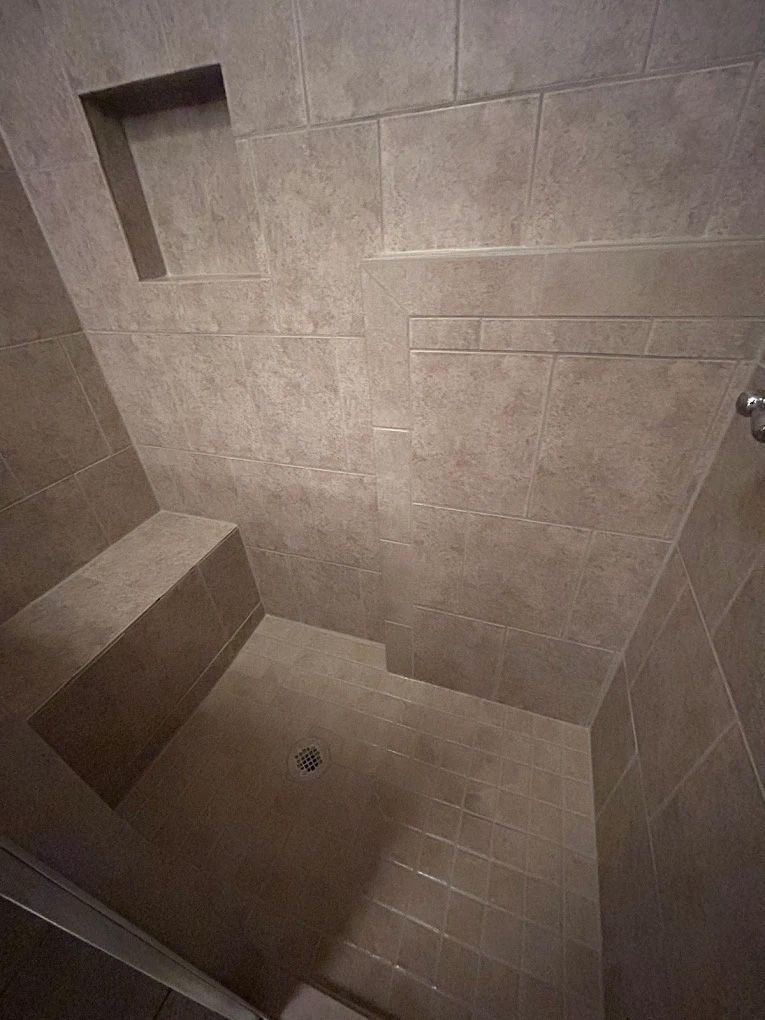 Shower with beige tiled walls, a built-in bench, and a rectangular storage niche.
