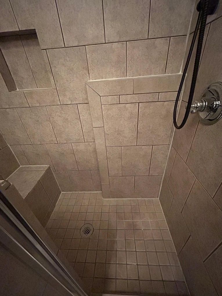 Beige tiled shower with angled design and handheld showerhead.