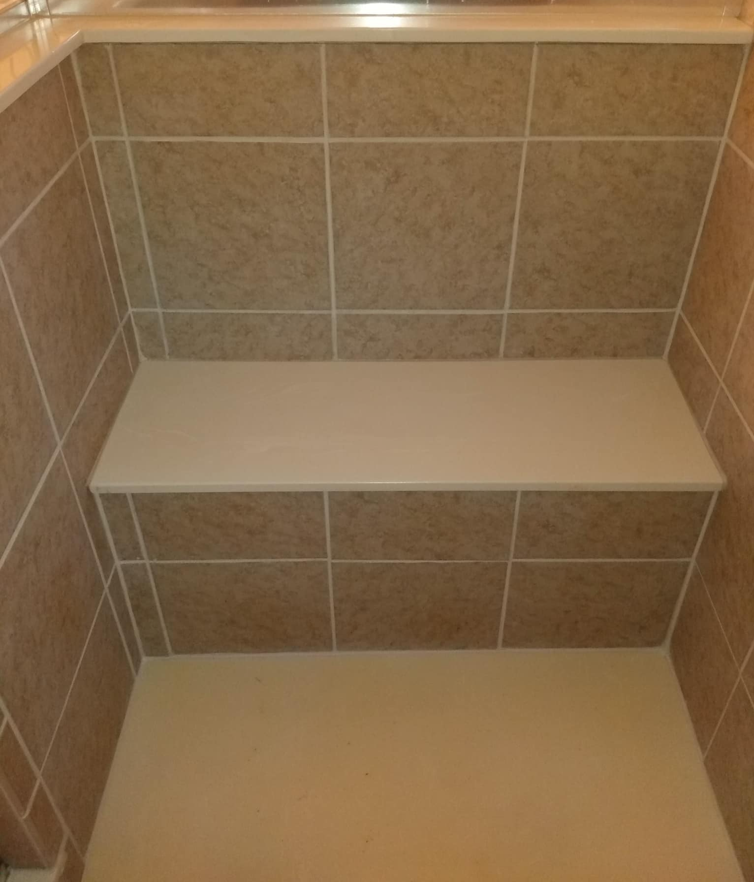 Shower stall with beige tile walls and a built-in bench.